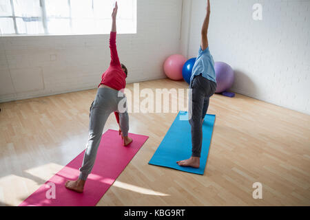 Hohe Betrachtungswinkel der Ausbilder mit weiblichen Kursteilnehmer üben Triangel pose im Yoga Studio Stockfoto