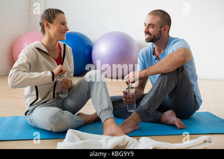 Ausbilder und Studentin reden, während sie Wasser im Yoga Studio Stockfoto