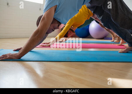 Seitenansicht der Lehrer mit den Schülern üben in den nach unten schauenden Hund Pose beim Yoga Studio Stockfoto