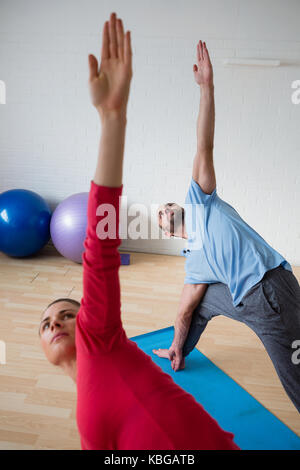 Männliche Kursleiter mit weiblichen Schüler üben triange Pose im Yoga Studio Stockfoto