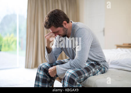 Betonte Mann auf dem Bett zu Hause sitzen Stockfoto