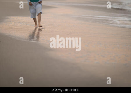 Ältere Frau zu Fuß am Strand bei Sonnenuntergang Stockfoto