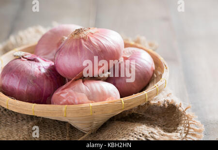 Rote Zwiebeln in Bambus Korb und auf Holz Hintergrund, Gemüse, die zum Kochen von Nahrungsmitteln Stockfoto