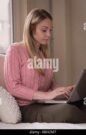 Junge Frau mit langem Haar mit Laptop auf dem Bett zu Hause. Stockfoto