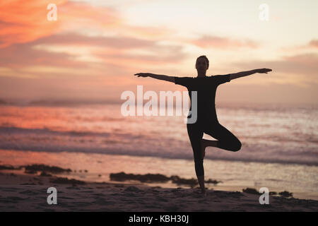 Schwangere Frau durchführen Yoga am Strand bei Sonnenuntergang Stockfoto