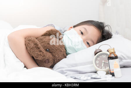 Krankes Mädchen mit hygienischen Maske zur Festlegung auf dem Bett, gesunde Konzept Stockfoto