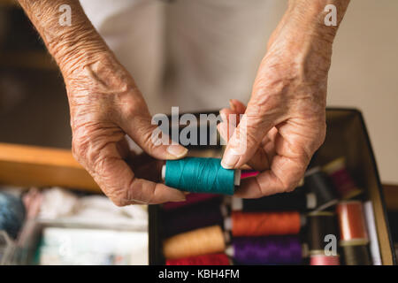 Nahaufnahme der älteren Frau threads zu Hause Holding Stockfoto