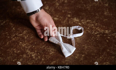Für den Bräutigam hand nimmt eine Fliege. Vorbereitung zum Hochzeitstag. Der Mann nimmt den Bow-tie. Hochzeit Zubehör. Bräutigam Holding braun Bow Tie in seiner Hand. Mann hält Fliege. Elegante Herren Kleidung. Hochzeit Stockfoto