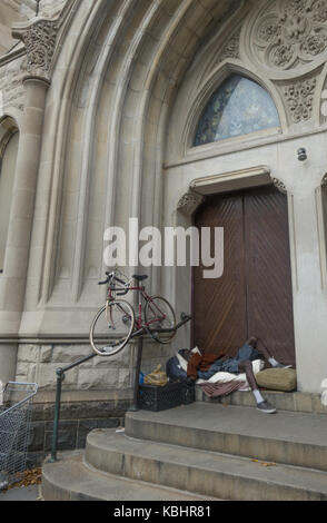 Obdachlosen Mann mit seinem Fahrrad schläft am Eingang der Kirche in die 7th Avenue in Park Slope, Brooklyn, NY. Stockfoto