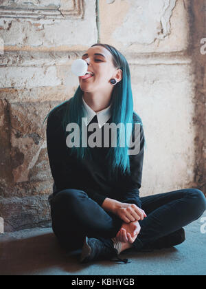 Cute gotischen Modell bläst bubblegum. Street Punk oder Hippie Studentin mit blau bunt gefärbte Haare, Piercing, Objektive, Ohren Tunnel und ungewöhnliche hairsty Stockfoto