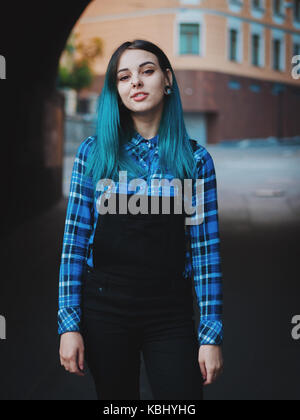 Street Punk oder Hippie Mädchen mit blau gefärbten Haaren. Frau mit Piercing in der Nase, violett Linsen, Ohren Tunnel und ungewöhnliche Frisur steht in der Stadt. Stockfoto