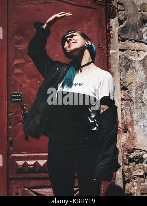 Street Punk oder Hippie Mädchen mit blau gefärbten Haaren. Frau mit Piercing in der Nase, violett Linsen, Ohren Tunnel und ungewöhnliche Frisur steht in der Stadt. Stockfoto