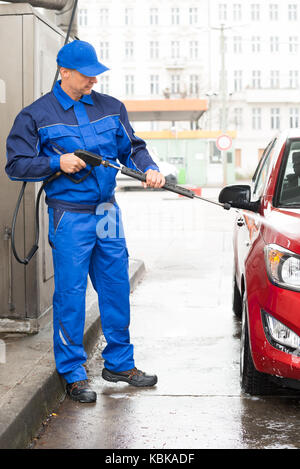 Reife Veteran mit Hochdruck-Wasserstrahl waschen rotes Auto an der Tankstelle Stockfoto