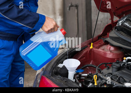 Zugeschnittenes Bild der Reifen serviceman gießen Scheibenwaschanlagenflüssigkeit in Auto Service station Stockfoto
