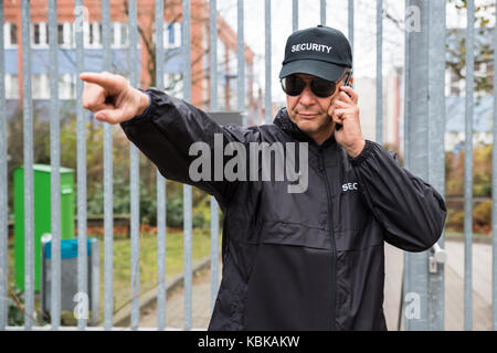 Ernsthafte Wachmann gestikuliert während der Verwendung von walkie-talkie vor Tor Stockfoto