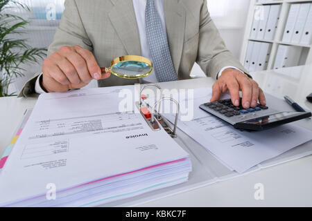 Mittelteil der männlichen Buchhalter mit Taschenrechner bei gedrückt gehaltener Lupe Wechsel im Amt zu analysieren Stockfoto