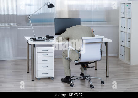 Ansicht der Rückseite des müde Geschäftsmann schlafen auf dem Schreibtisch im Büro Stockfoto