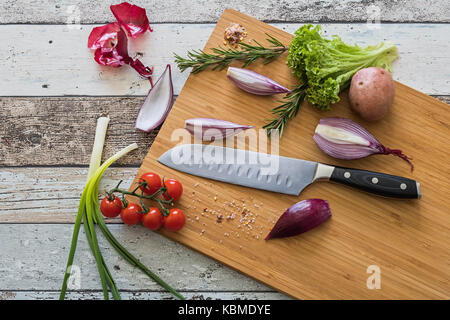 Messer mit gesunden Lebensmitteln - Gemüse, Zwiebeln, Salat, Tomaten, Kartoffeln auf einem Schneidebrett mit Holz Hintergrund Draufsicht platziert Stockfoto