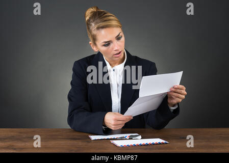 Entsetzte Geschäftsfrau lesen schreiben am Schreibtisch über grauer Hintergrund Stockfoto