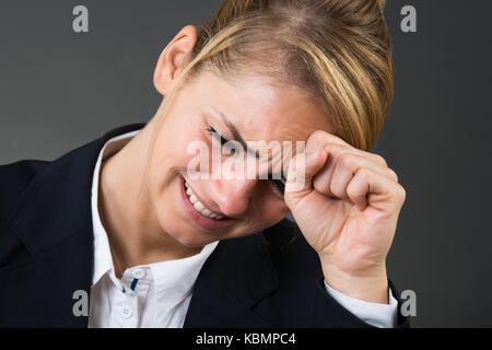 Deprimiert junge geschäftsfrau schlagende Hand auf den Kopf über grauer Hintergrund Stockfoto