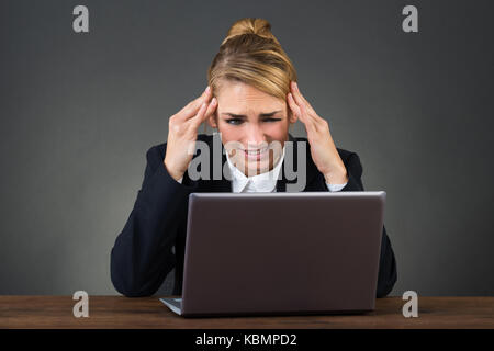 Junge Geschäftsfrau leiden unter Kopfschmerzen am Schreibtisch über grauer Hintergrund Stockfoto