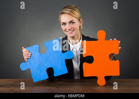 Portrait von lächelnden Geschäftsfrau holding Puzzleteile am Schreibtisch über grauer Hintergrund Stockfoto