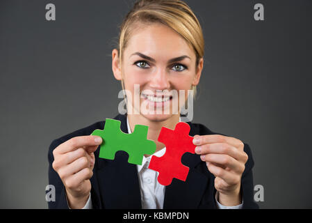 Portrait von lächelnden Geschäftsfrau holding Puzzleteile am Schreibtisch über grauer Hintergrund Stockfoto