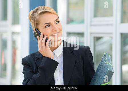 Lächelnden jungen Geschäftsfrau mit Handy während Weg suchen Stockfoto