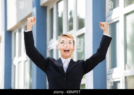 Happy Geschäftsfrau Anheben der Arme Erfolg mit dem Gebäude im Hintergrund zu feiern. Stockfoto