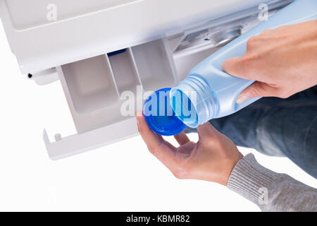 Woman's Hand gießt flüssiges Reinigungsmittel im Deckel mit Waschmaschine im Hintergrund Stockfoto