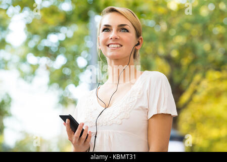 Lächelnden jungen Frau Hören von Musik über Kopfhörer mit Handy Stockfoto