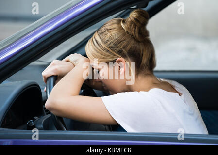 Seitenansicht der Müde junge Frau Schiefen am Lenkrad im Auto. Stockfoto