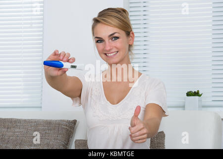 Porträt der glückliche junge Frau, die Gestik, die Daumen hoch, während positive Schwangerschaft führen zu Hause angezeigt Stockfoto