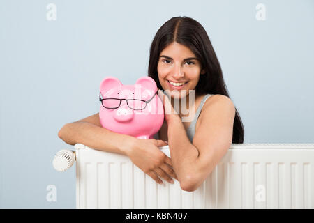 Junge Frau lehnte sich auf den Kühler mit rosa Sparschwein zu Hause Stockfoto