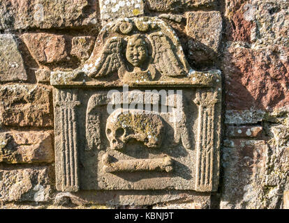 Nahaufnahme eines abgenutzten Grabsteins mit Totenkopf und Kreuzknochen und Engel auf dem Dorffriedhof von Stenton, East Lothian, Schottland, Großbritannien Stockfoto