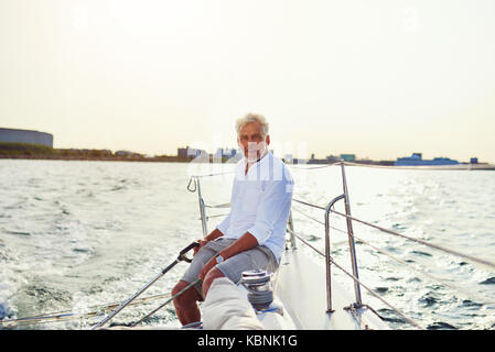 Reifer Mann sitzen auf dem Deck des Bootes und geniessen Sie einen sonnigen Tag Segeln entlang der Küste Stockfoto