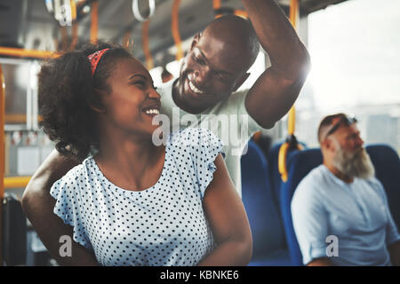 Lächelnden jungen afrikanischen Paar lachend und umarmen einander beim zusammen auf einem Bus Stockfoto
