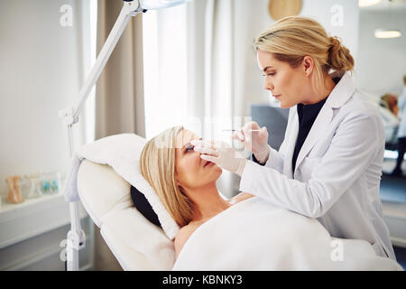 Junge Ärztin durchführen Botox Injektionen auf der Stirn eine reife Frau lag auf einem Tisch in einer Schönheitsklinik Stockfoto