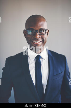 Porträt eines lächelnden jungen afrikanischen Geschäftsmann in Anzug und Brille allein in einem Büro Stockfoto