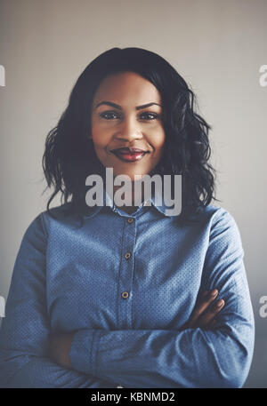 Porträt einer jungen afrikanischen Geschäftsfrau, Lächeln, während allein in einem Büro mit verschränkten Armen Stockfoto
