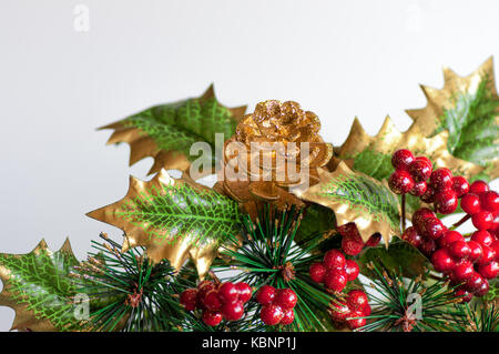 Weihnachten Dekoration, bestehend aus künstlichen goldene Tannenzapfen und Holly mit roten Beeren. weißen Hintergrund. Stockfoto