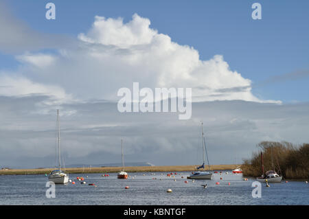 Yachten festgemacht am Fluss Stour bei Christchurch unter einem dramatischen Himmel. Die Isle of Wight ist im Hintergrund sichtbar. Stockfoto