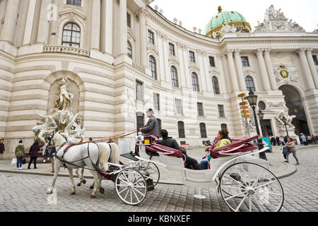 Berühmte Pferdekutsche genannt Fiaker führt an der Hofburg am Michaelerplatz in Wien mit Touristen und Menschen. Stockfoto