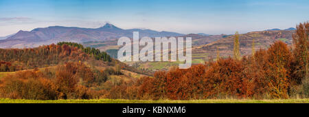 Wunderschöne Herbst Landschaft Panorama in die Berge. Wald mit rotem Laub auf sanften Hügeln, Dorf im Tal und Bergrücken mit High Peak in Einem Stockfoto