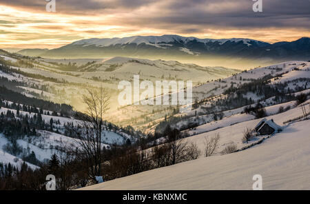 Wunderschöne Landschaft in den Bergen bei Sonnenaufgang. Dorf und ländlichen Felder auf die Hänge des Tals mit Schnee/ im Morgenlicht abgedeckt Stockfoto