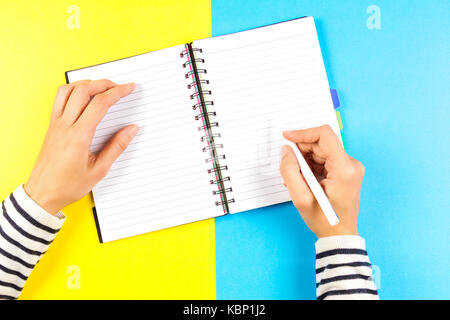 Frau Hand schreiben im Notebook über Blau und Gelb Hintergrund. top View Stockfoto