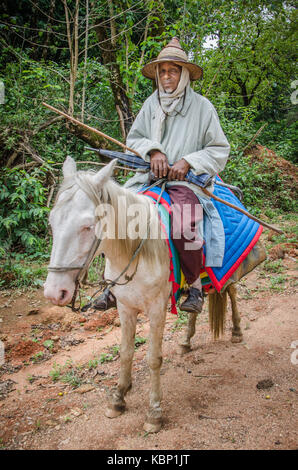KAMERUN - 26. MÄRZ 2014: Unidentifizierter Fulani-Mann in traditioneller Kleidung mit breitem Hut auf seinem weißen Pferd, Ringstraße, Zentralafrika Stockfoto