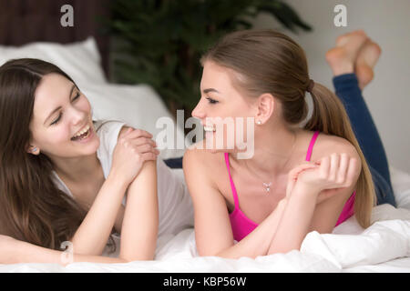 Zwei junge lächelnde Freundinnen liegend auf Bett und Chatten. Stockfoto