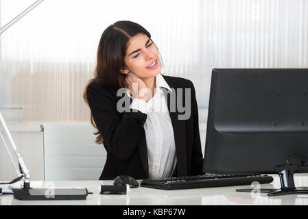 Junge Geschäftsfrau Nackenschmerzen leiden während der Arbeit am Schreibtisch im Büro Stockfoto