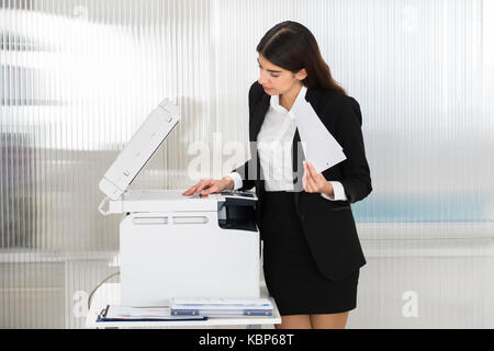 Junge Geschäftsfrau mit Kopierer im Büro Stockfoto